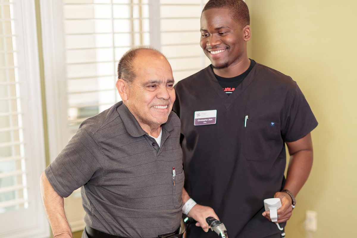 Caregiver assisting a resident with walker therapy at Arlington Gardens Care Center
