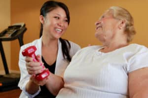 Caregiver assisting elderly woman with light weight exercise at Arlington Gardens Care Center