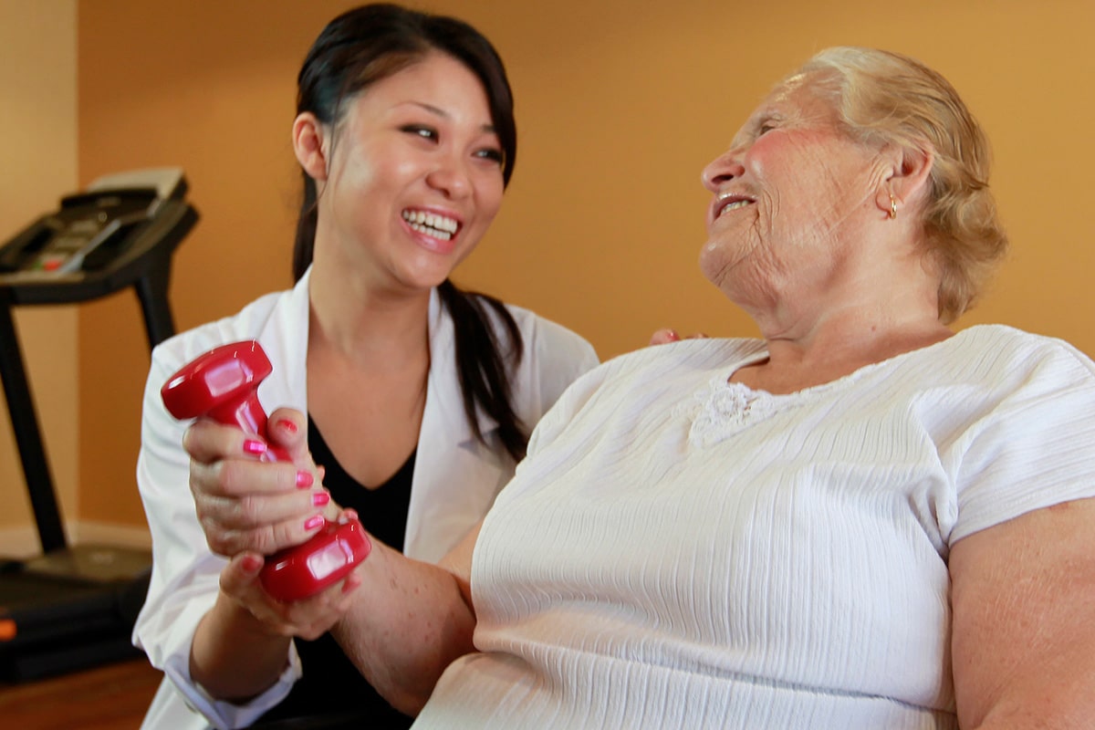 Caregiver assisting elderly woman with light weight exercise at Arlington Gardens Care Center